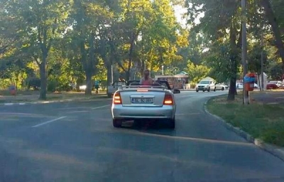 În picioare, pe bancheta din spate a decapotabilei, în trafic